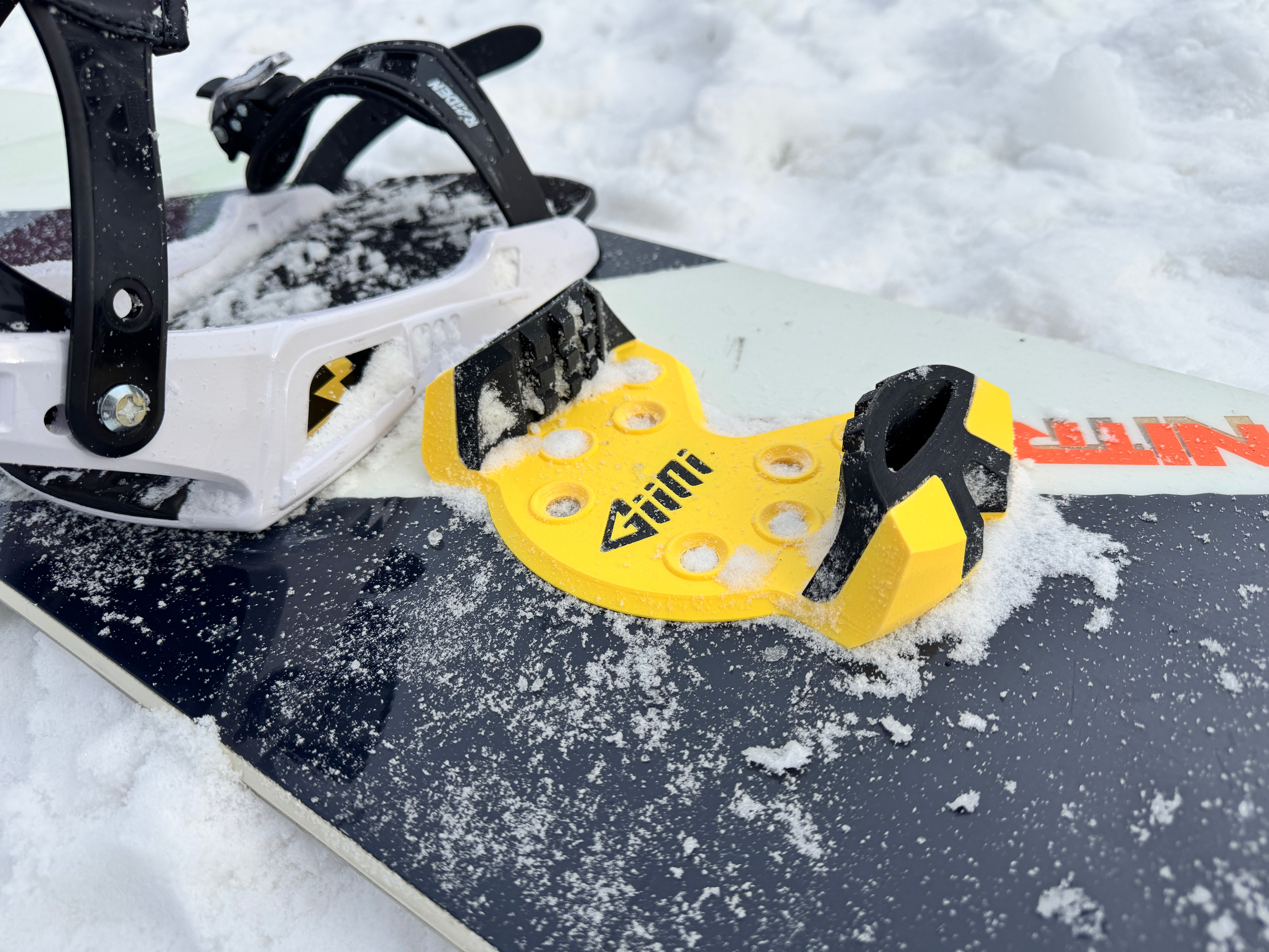 Giini Pyro Hazard fitted on a snowboard between white bindings, on-snow close-up