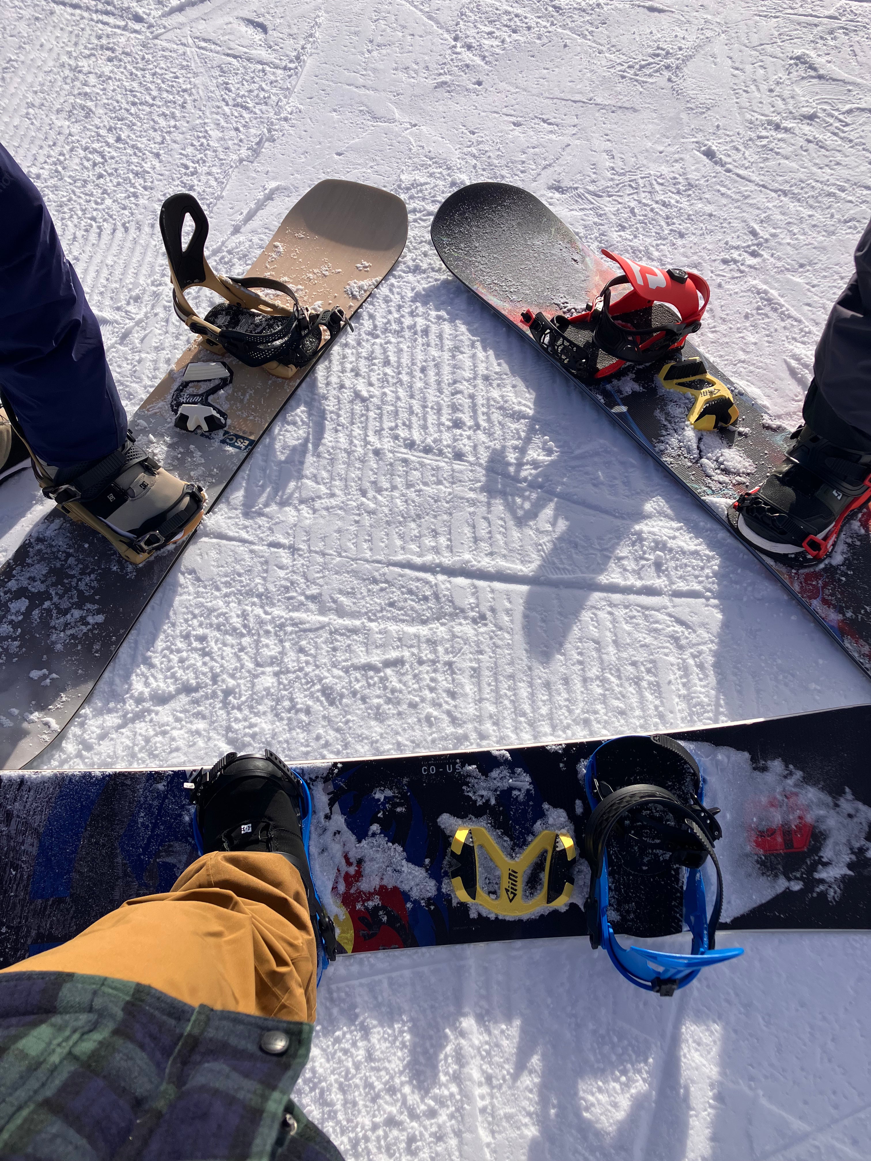Top-down view of three snowboards on the snow between riders, fitted with Giini Pyros