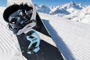 Giini Pyro Glacier Blue mounted on a snowboard tipped up on corduroy snow, alpine peaks in the background