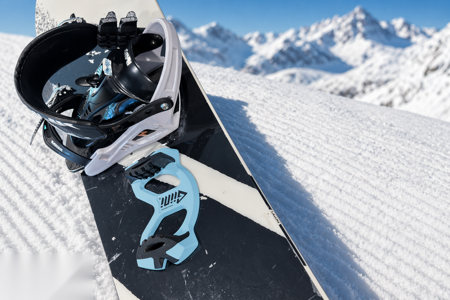 Giini Pyro Glacier Blue mounted on a snowboard tipped up on corduroy snow, alpine peaks in the background