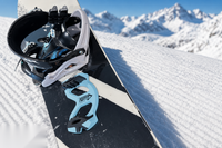 Giini Pyro Glacier Blue mounted on a snowboard tipped up on corduroy snow, alpine peaks in the background