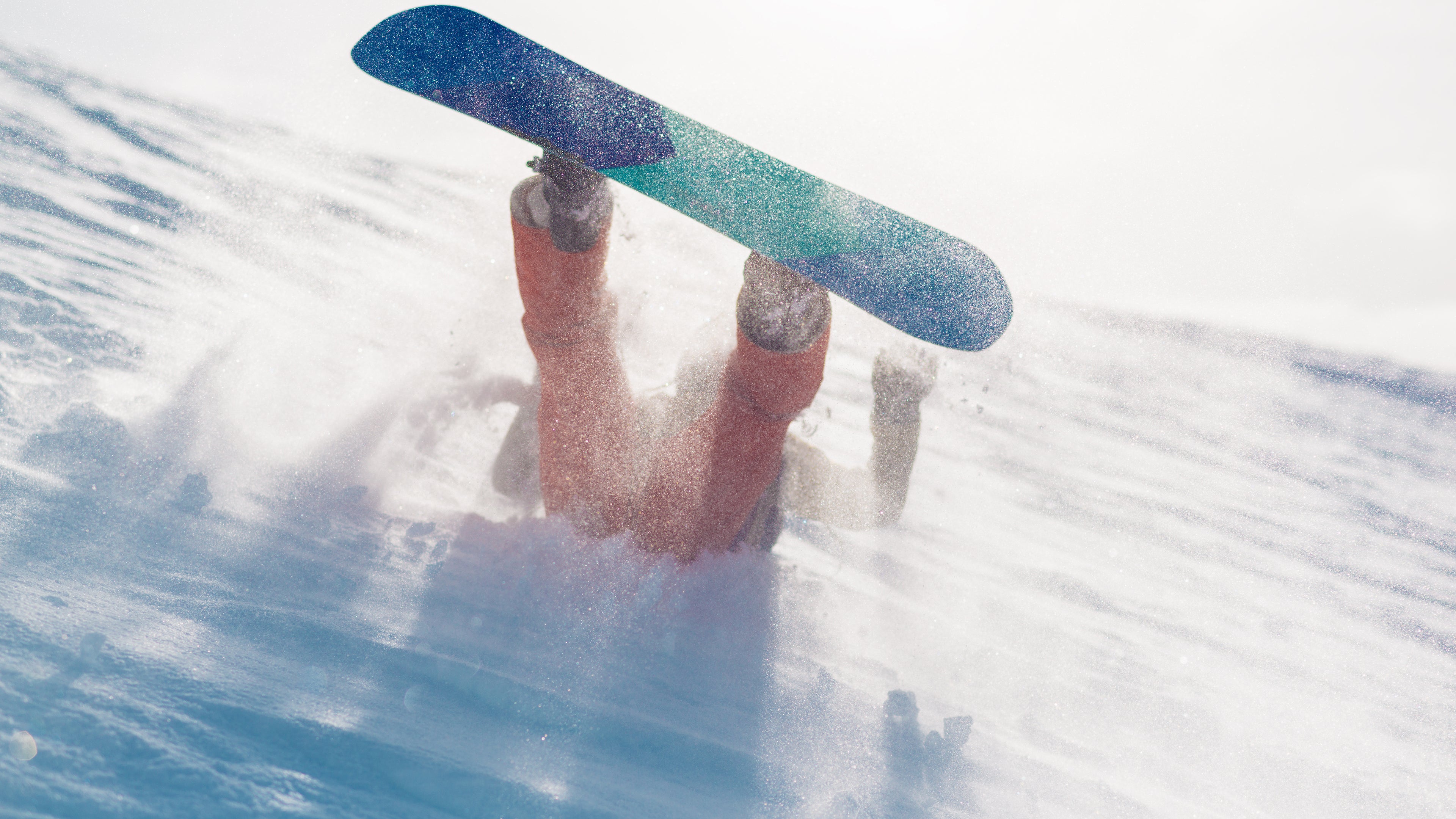 Snowboarder crashing into deep powder mid-fall, board kicked up in the air